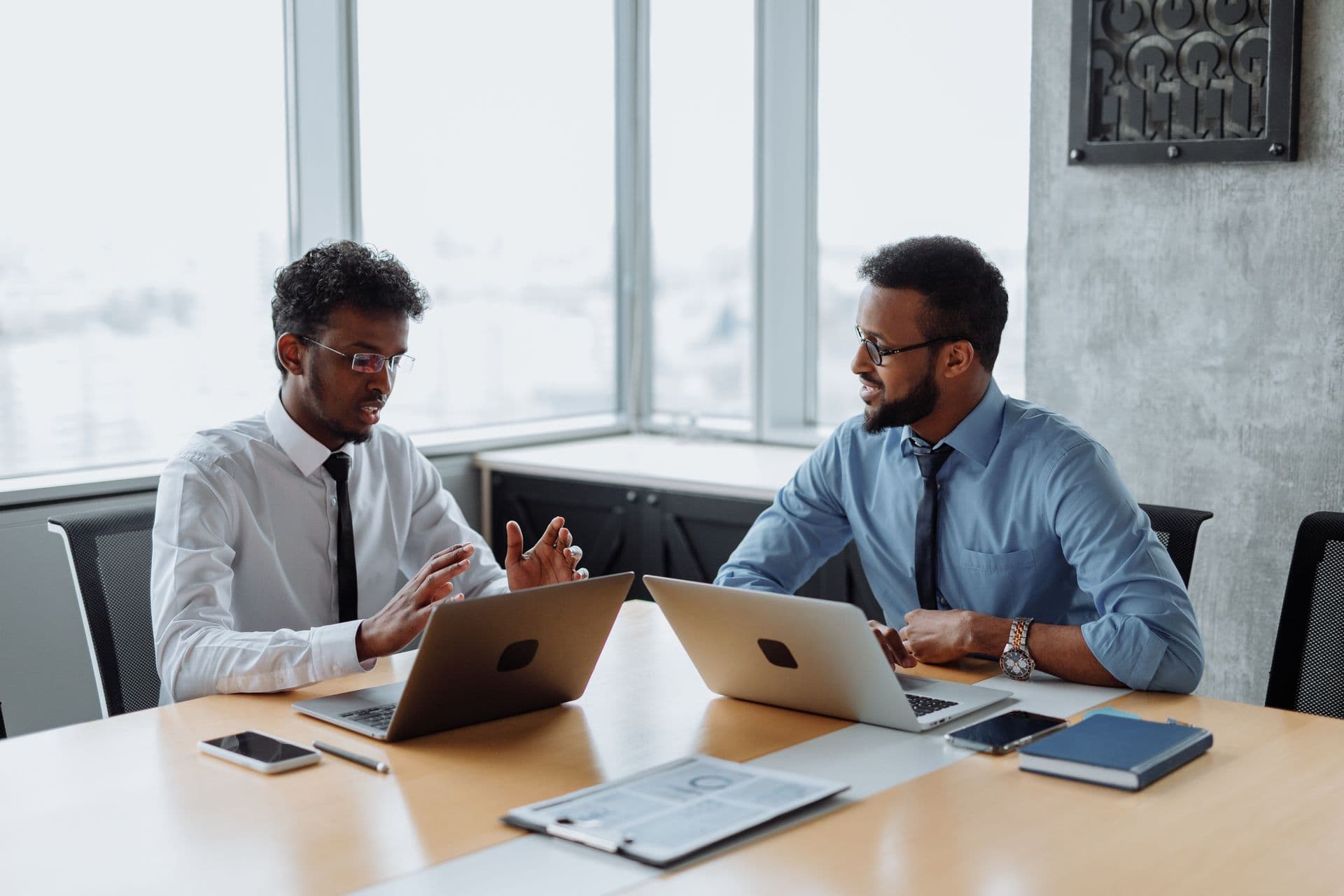 Two professionals in discussion at a table with laptops.